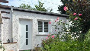 Een wit huis met een witte deur en luiken, een pad van baksteen en een tuin met roze bloemen.