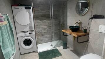 Een kleine badkamer met een wasmachine, douchecabine, wastafel met spiegel en toilet.