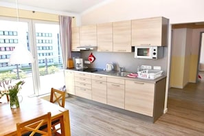 A modern kitchen with wooden cabinets, a microwave, and a dining area with a table and chairs. - Apartment near the beach in Fehmarn-Burgtiefe (Fehmarn OT Burgtiefe-Südstrand)