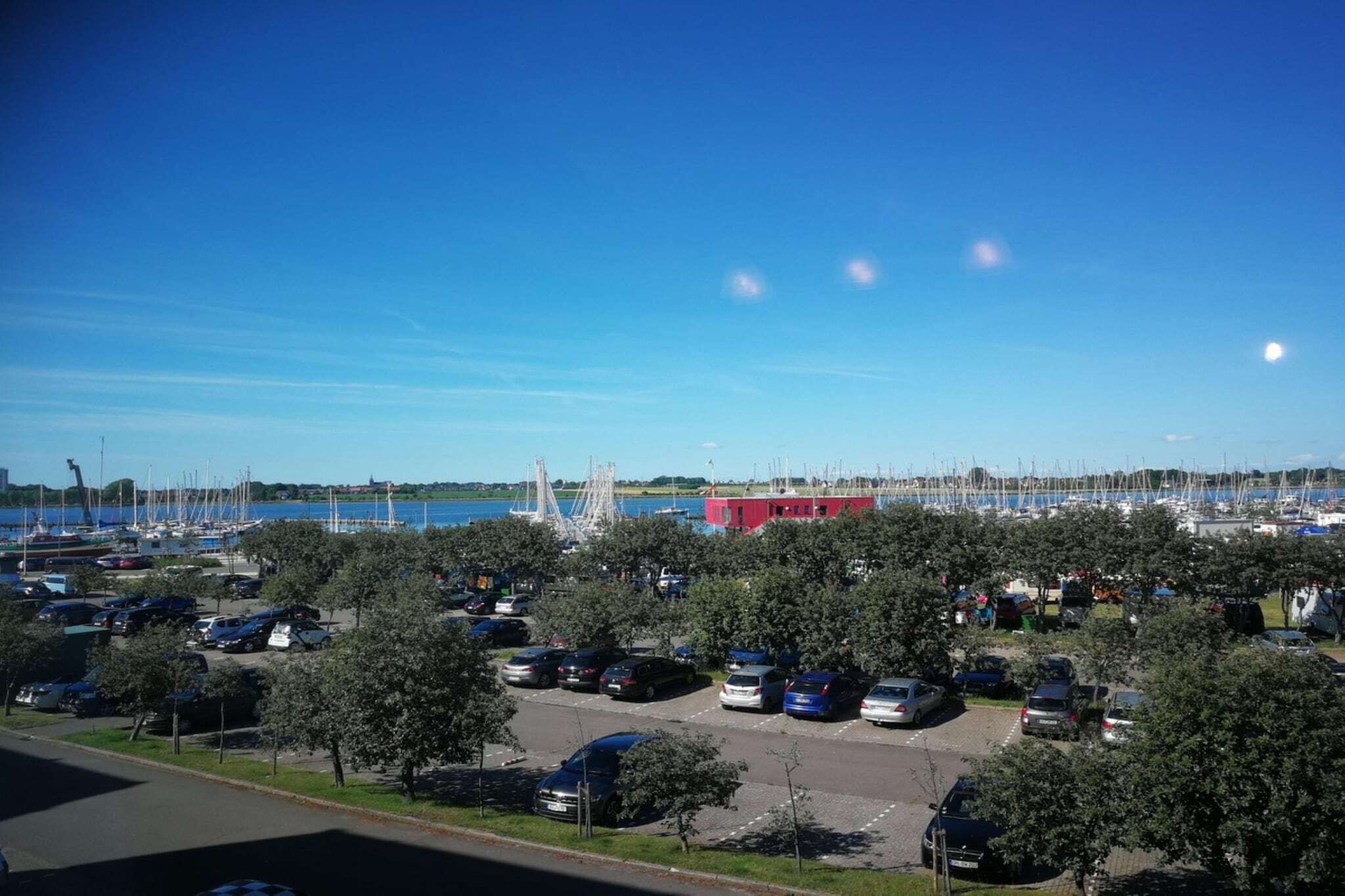 A marina with boats, a red building, and a parking lot with cars.