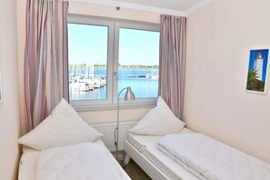 Ein Zimmer mit zwei Betten, einem Fenster mit Blick auf Boote und Wasser, und einem Gemälde an der Wand.