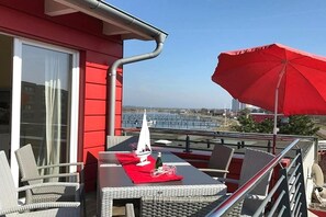 An outdoor dining area with a table, chairs, and a red umbrella. - Apartment Fehmarn-Burgtiefe (Fehmarn OT Burgtiefe-Südstrand)