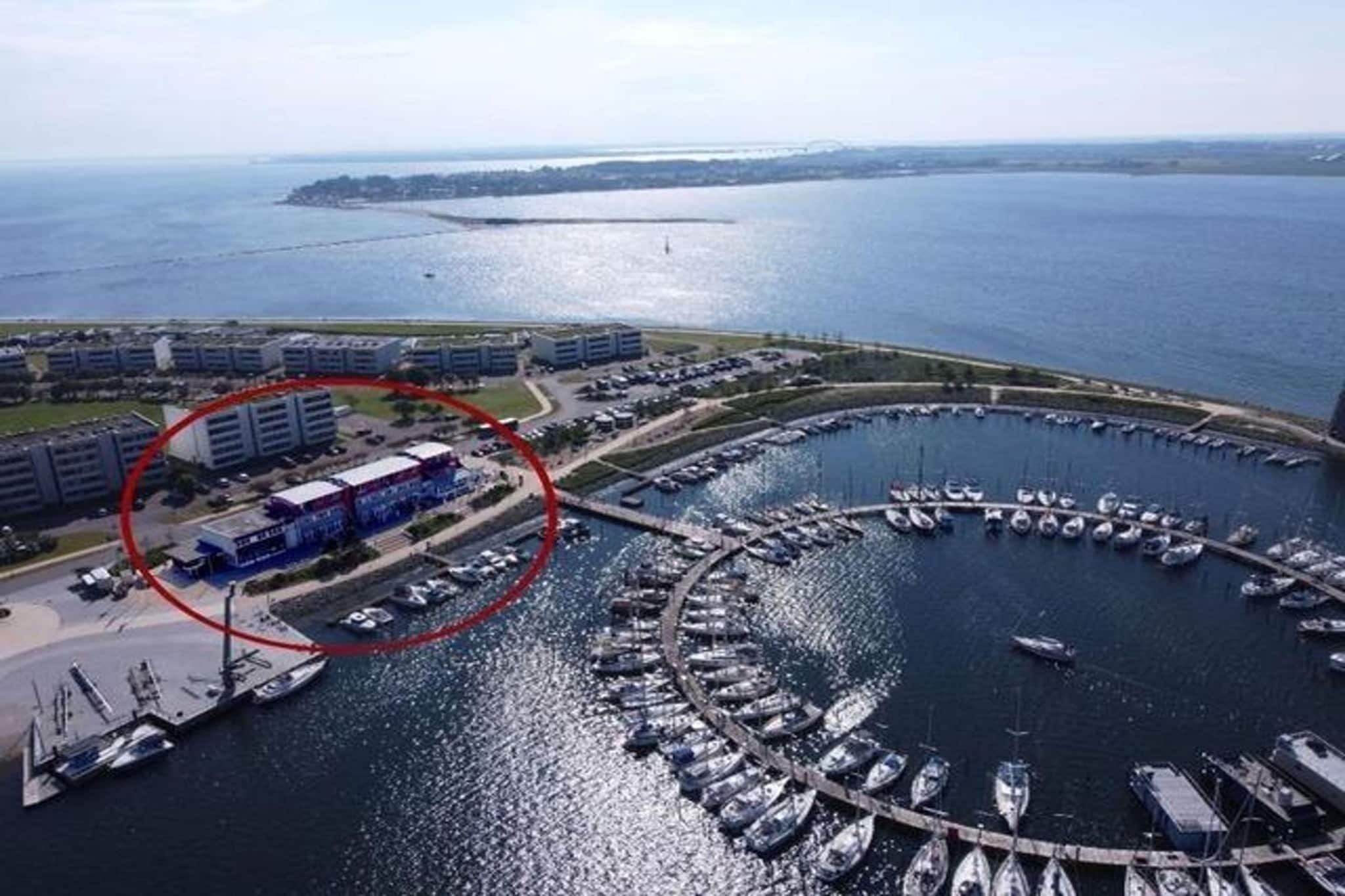 A marina with boats docked, a parking area, and buildings in the background.