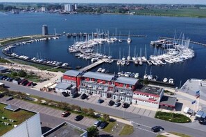 A marina with boats docked in a circular pattern, a red building with a flat roof, and a parking area with cars. - Apartment Fehmarn-Burgtiefe (Fehmarn OT Burgtiefe-Südstrand)