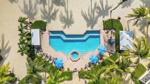 Ein Luftbild eines Resorts mit einem zentralen Schwimmbecken, umgeben von Palmen und Liegestühlen.