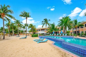 A resort with a swimming pool, sun loungers, and palm trees. - Kaibo Yacht Club  2 Bdr Beachfront Condo Hot Tub and Pool (Rum Point)
