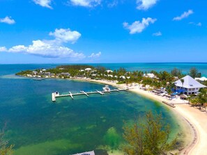 An aerial view of a coastal resort with a pier extending into the water, surrounded by lush greenery and beachfront villas. - Kaibo Yacht Club  2 Bdr Beachfront Condo Hot Tub and Pool (Rum Point)