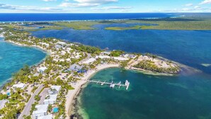 Vista aérea de um resort costeiro com águas cristalinas, um píer e diversos edifícios.