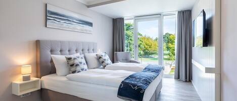 A modern bedroom with a large bed, bedside tables, a flat-screen TV, and a view of the outdoors.