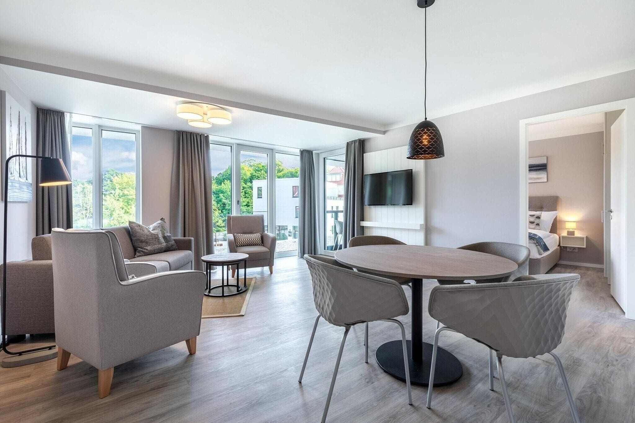 A modern living room with a dining area, large windows, and a flat-screen TV.