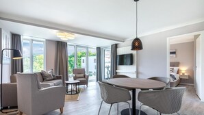 A modern living room with a dining area, large windows, and a flat-screen TV. - Deluxe Baltic Stay für 6 Personen (Travemünde)