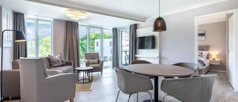 A modern living room with a dining area, large windows, and a flat-screen TV.