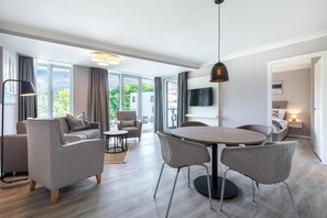 Ein modernes Wohnzimmer mit Essbereich, großen Fenstern und einem Flachbildfernseher.