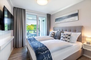 A modern bedroom with a large bed, a flat-screen TV, a balcony view, and a painting on the wall. - Deluxe Baltic Stay für 6 Personen (Travemünde)