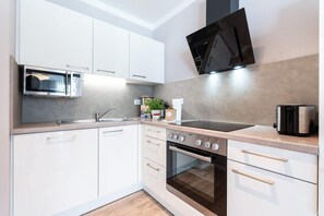 A modern kitchen with white cabinetry, a built-in microwave, a stove, and a black range hood. - Deluxe Baltic Stay für 6 Personen (Travemünde)