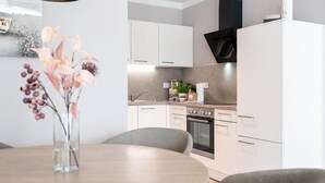 A modern kitchen with white cabinets, a black range hood, and a dining area with a table and chairs. - Deluxe Baltic Stay für 6 Personen (Travemünde)