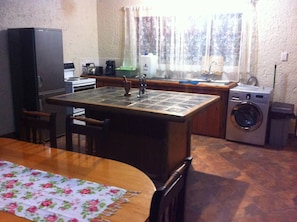 A compact kitchen with a central island, a washing machine, and a refrigerator. - Green Fountain Villa 5 (Port Alfred)