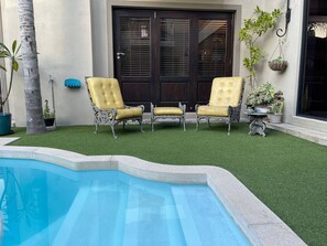 A pool with artificial grass, two yellow chairs, and a dark wooden door. - Guest suite Sunset Beach, Milnerton 85m2 (Milnerton)