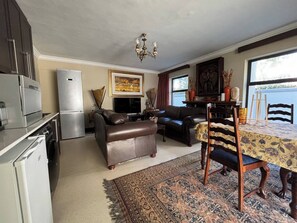 A compact living space with a kitchenette, a sofa, a dining table with chairs, and a patterned rug. - Guest suite Sunset Beach, Milnerton 85m2 (Milnerton)