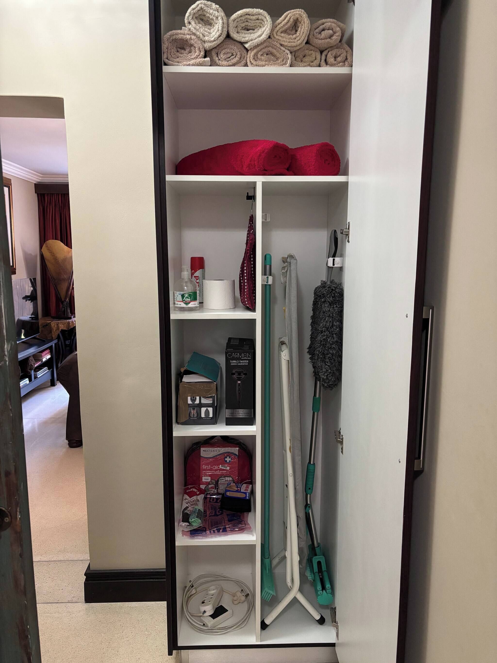 Een hotelkamer met een kledingkast met handdoeken, een verbanddoos, schoonmaakmiddelen en een stofzuiger.