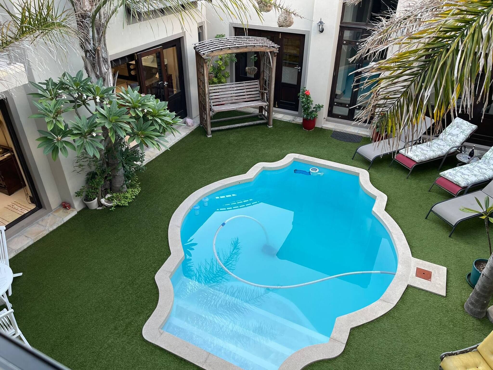 Una piscina rodeada de césped artificial, con sillas de descanso y plantas en macetas.
