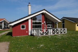 A red building with a white porch and a chimney, number 152, in a grassy area with other buildings. - Strandhaus mit Spa-Bereich (Großenbrode)