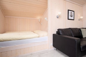 Ein kleiner Raum mit Holzwänden, einem Bett, einer schwarzen Ledersofa und zwei Wandleuchten.