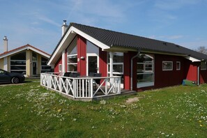 A red building with a white porch and a car parked in front. - Strandhaus mit Spa-Bereich (Großenbrode)