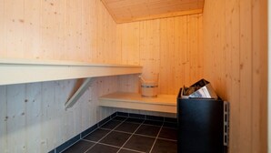 En bastu med träväggar, ett kaklat golv, en hylla och en papperskorg.