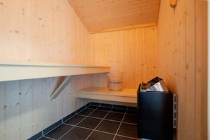 Eine Sauna mit Holzwänden, gefliestem Boden, Ablagefläche und Mülleimer.