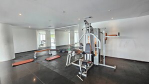 Un gimnasio con varios equipos de ejercicio, incluyendo una prensa de banca, una estructura para sentadillas y una máquina de poleas.