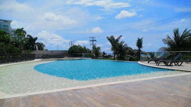 Una piscina con zona de madera rodeada de palmeras y un cielo despejado.
