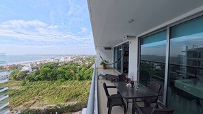 Un balcone con tavolo e sedie, un'amaca e vista sull'oceano e sullo skyline della città.