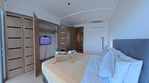 Una camera da letto moderna con un letto, una TV montata a parete, un armadio in legno e un tavolino con una pianta e una ciotola di frutta.