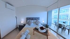 A modern hotel room with a large bed, bedside tables, a small table with a bowl of fruit, and a view of the city through large windows. - Beautifull Condo Apartament with sea view Morros Sonesta (Cartagena)
