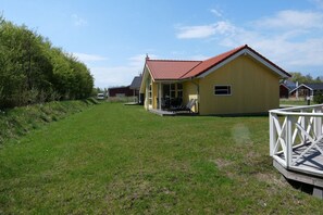 A yellow building with a red roof, a covered patio with chairs, and a white fence. - Grobenbrode Haven mit gemütlichem Kamin (Großenbrode)