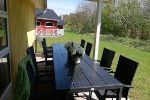 An outdoor patio with a table and chairs, a flower vase, and a view of a red barn in the background. - Grobenbrode Haven mit gemütlichem Kamin (Großenbrode)