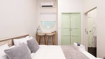 A bedroom with a bed, bedside tables, a desk, an air conditioner, a green door, and a bathroom with a marble floor.