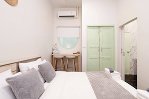 A bedroom with a bed, bedside tables, a desk, an air conditioner, a green door, and a bathroom with a marble floor. - Spacious Heritage House Prime Location Family Stay (Khet Bang Rak)