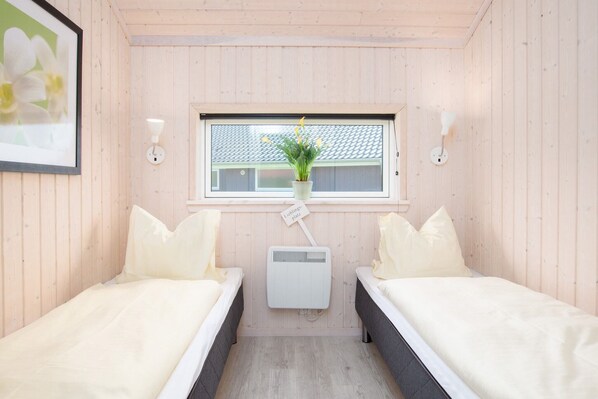 Una habitación con dos camas, una ventana con planta y un pequeño calentador.