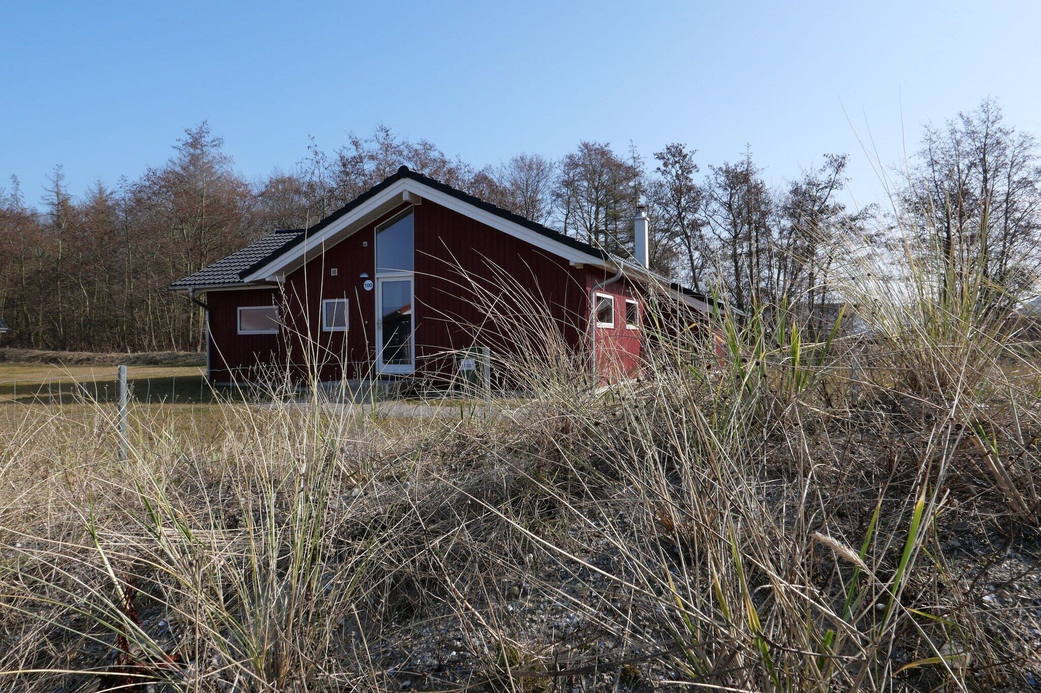 Un bâtiment rouge avec un toit en pente, entouré de hautes herbes et d’arbres.