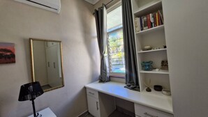 Um quarto com escrivaninha, espelho, estante e ar condicionado.