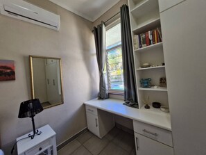 Ein Zimmer mit Schreibtisch, Spiegel, Bücherregal und Klimaanlage.