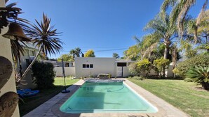 Uma piscina com deck ladrilhado, rodeada por um gramado e palmeiras.