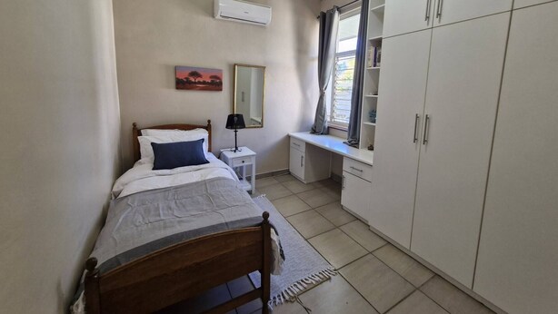 Quarto com cama, mesa de cabeceira, espelho, guarda-roupa e janela com cortinas.