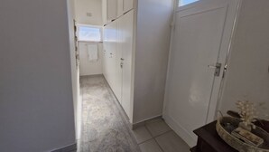 Corredor que dá para um banheiro com janela, porta e um porta-toalhas.