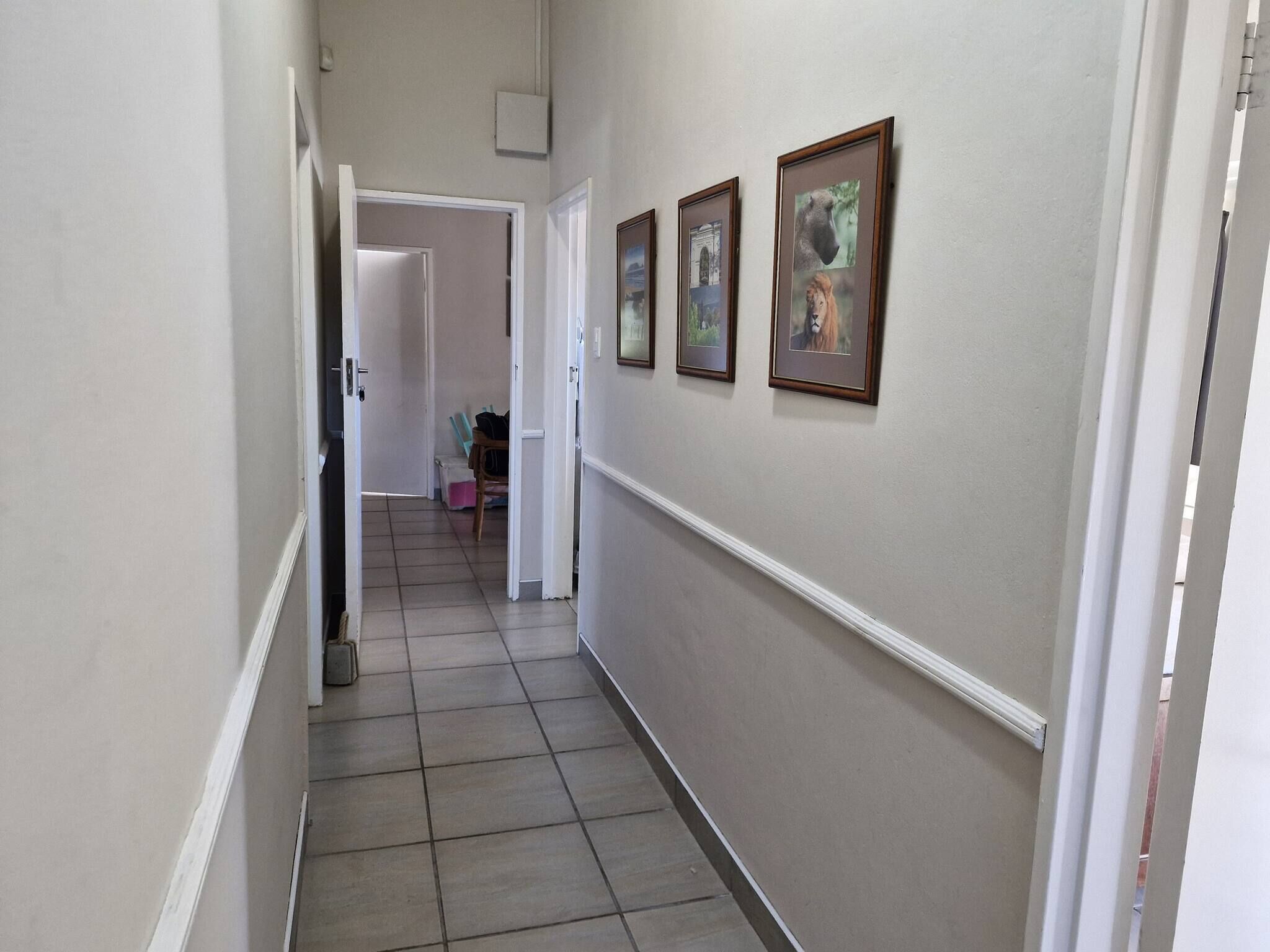 Un couloir avec un sol carrelé, des murs blancs et des tableaux encadrés sur le côté droit.