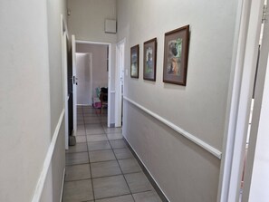 A hallway with a tiled floor, white walls, and framed pictures on the right.