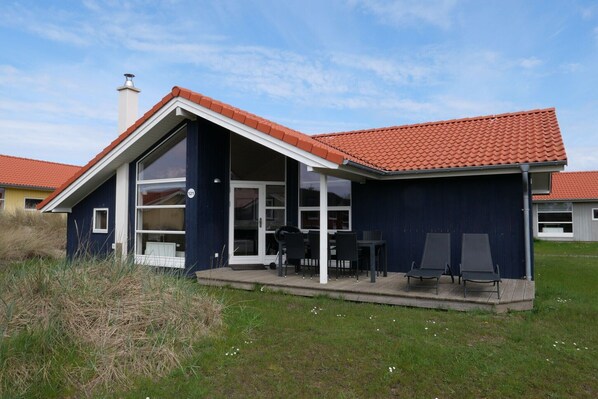 A modern house with a large glass window, a covered patio with outdoor furniture, and a red-tiled roof. - Grobenbrode Villa mit hauseigenem Spa (Großenbrode)