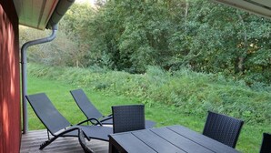 Eine Terrasse im Freien mit einem Holztisch und vier Stühlen, umgeben von viel Grün.